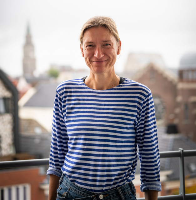 Witte vrouw met streepjesshirt staat op een balkon met achter haar een stukje skyline van de stad Groningen.