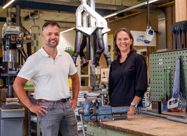 Een witte man en een witte vrouw in een leslokaal van Alfa-college. Ze lachen allebei. Om hen heen zijn gereedschap, machines en werkbanken.