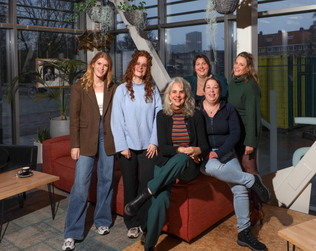 Zes witte vrouwen poseren op en naast een bank.