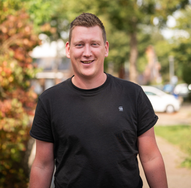 Witte man met zwart shirt loopt door een zonnige en groene woonwijk