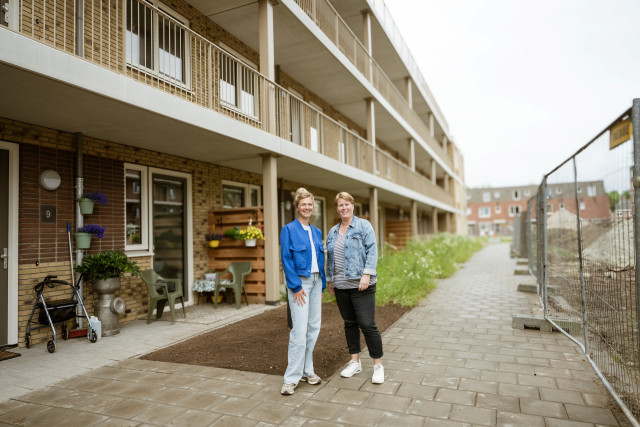Twee witte vrouwen bij nieuwbouwflats. Rechts nog een bouwhek en modder.