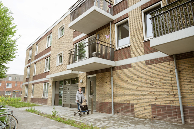 Oude witte vrouw met een rollator loopt voor een nieuwbouwflat.