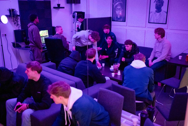 Een groep jongemannen in een geluidsstudio. Er zijn veel hoodies en witte bekertjes