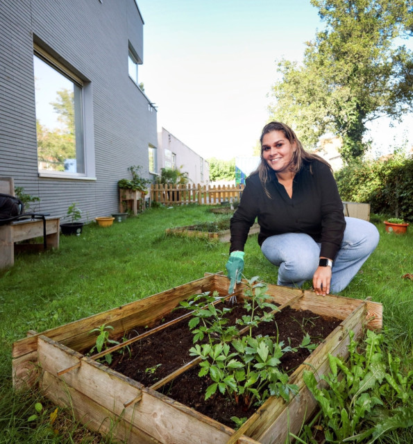 Vrouw op haar hurken met een kleine schoffel bij een moestuintje