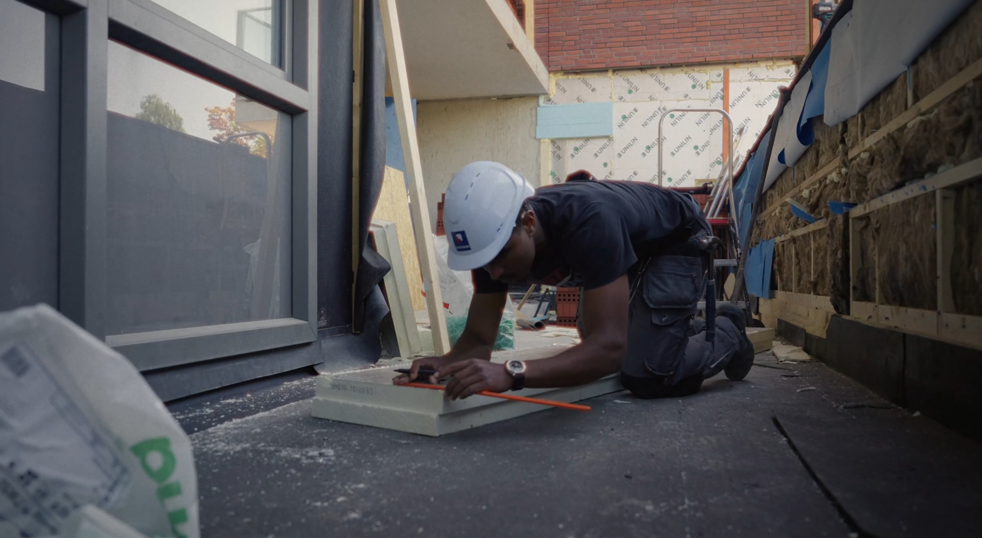 De AanDeBak-garantie film over Stephanos. Een still uit de video over dit project. Daarop is een donkere man te zien die iets aan het uitmeten is. Hij draagt een witte bouwvakkershelm.