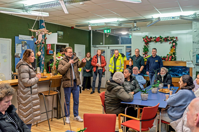 Witte man spreekt diverse groep mensen toe in een buurtcentrum