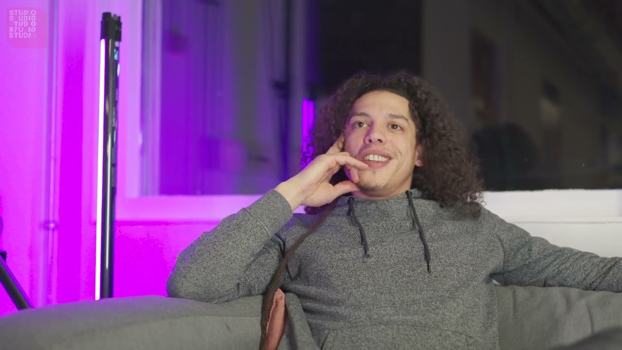 Een beeld uit een video over de open studio in Selwerd. Je ziet een jongen met lang krulhaar op een bank zitten.