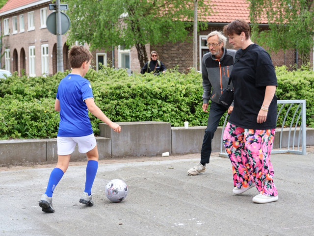 Stenen voetbalveldje met daarop twee volwassenen en een kind
