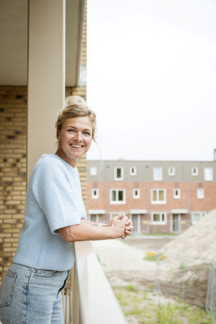 Witte vrouw met opgestoken blond haar leunt op een galerij-leuning.