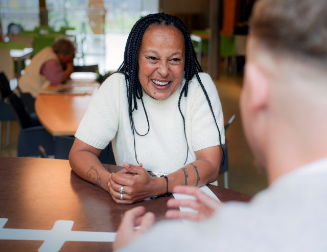 Donkere vrouw met dreads en wit shirt praat met witte man die je op de rug ziet,