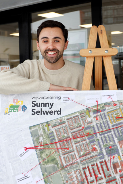 Witte man met lichtgekleurde trui hangt over een bord met uitleg op een schildersezel.