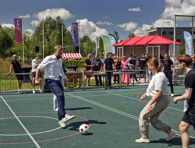 Witte man voetbalt met jongeren op een sportveldje.