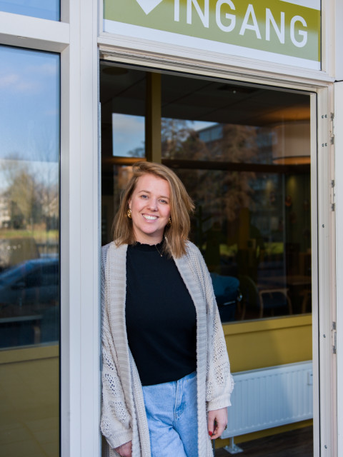 Witte vrouw lacht naar de camera in een deuropening