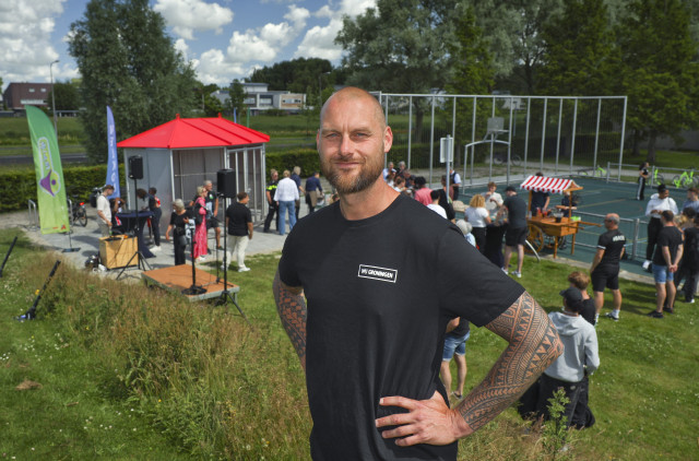 Witte man Twan Grommers in zwart shirt met wit logo WIJ Groningen. Staat op een heuveltje met daarachter de nieuwe hangplek en het sportveldje