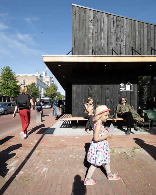 Houten wijkgeboutje met op de voorgrond een blond kind in een jurkje.